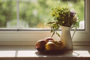 Sanftes Fensterlicht beleuchtet Obstschale und Blumenkrug auf einer Fensterbank