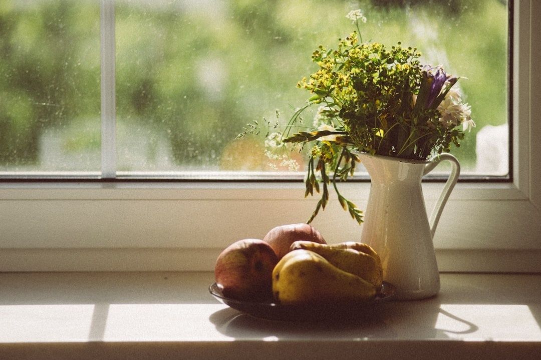 Sanftes Fensterlicht beleuchtet Obstschale und Blumenkrug auf einer Fensterbank