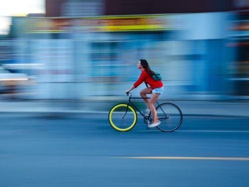 Radfahrerin mit rotem Oberteil fährt vor verschwommener Stadtkulisse